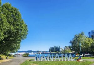 beautiful sunny day in Nanaimo habour front, with a big Nanaimo sign, and lush green trees.