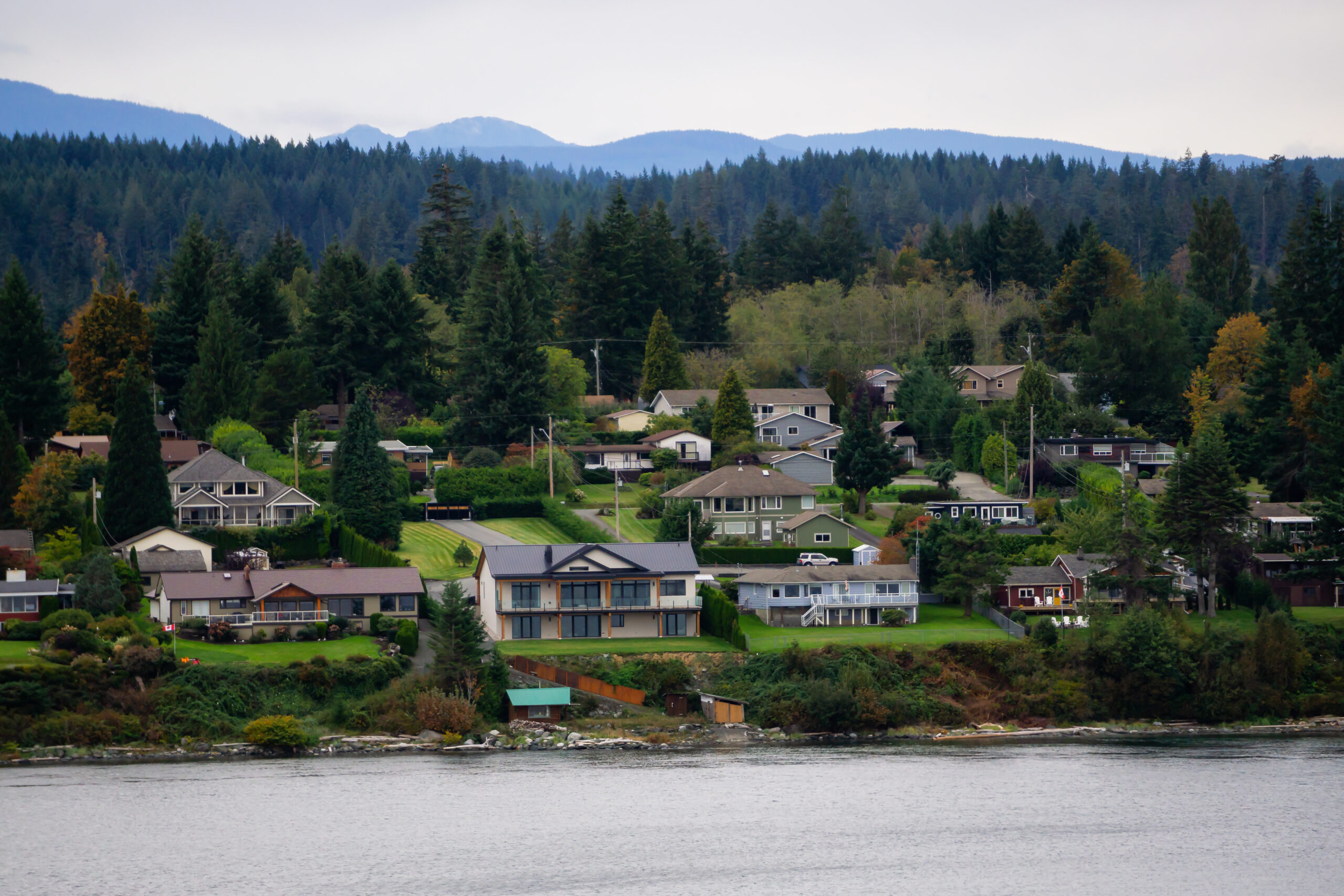 Multiple-level luxury homes with ocean views built into a forested hillside overlooking Hammond Bay, Nanaimo, with mountains in the background