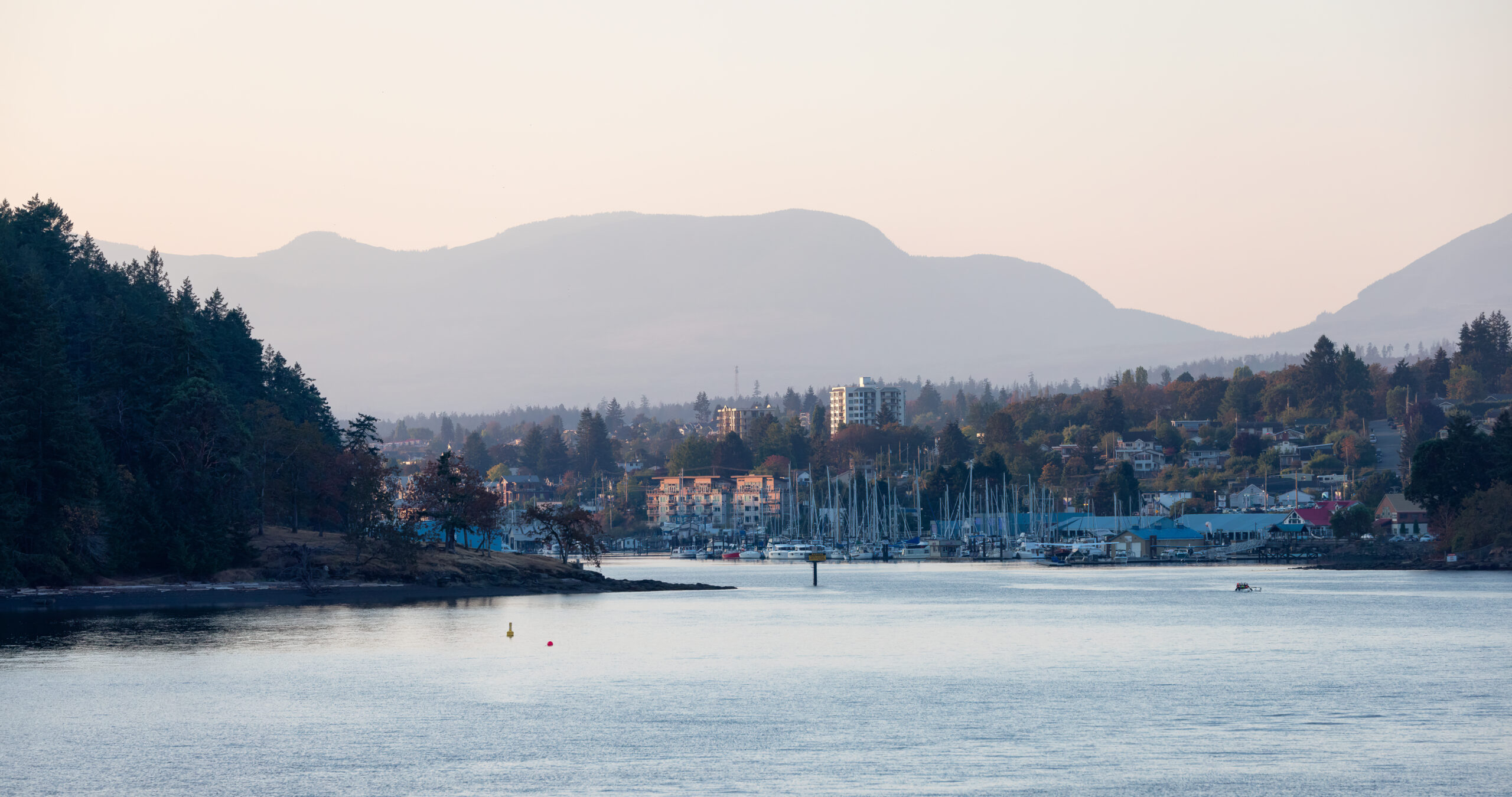 Residential properties cascading down a hillside with waterfront views, surrounded by evergreen forests and mountains in Hammond Bay, Nanaimo